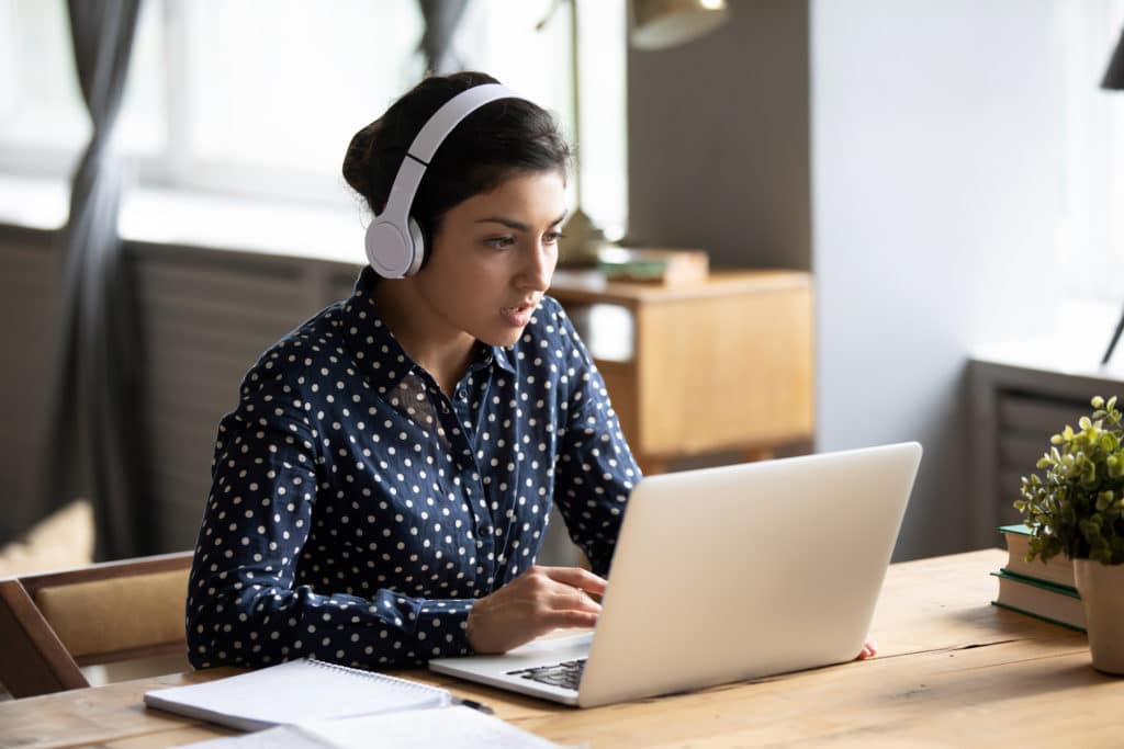 Female university student wearing headphones uses laptop in library