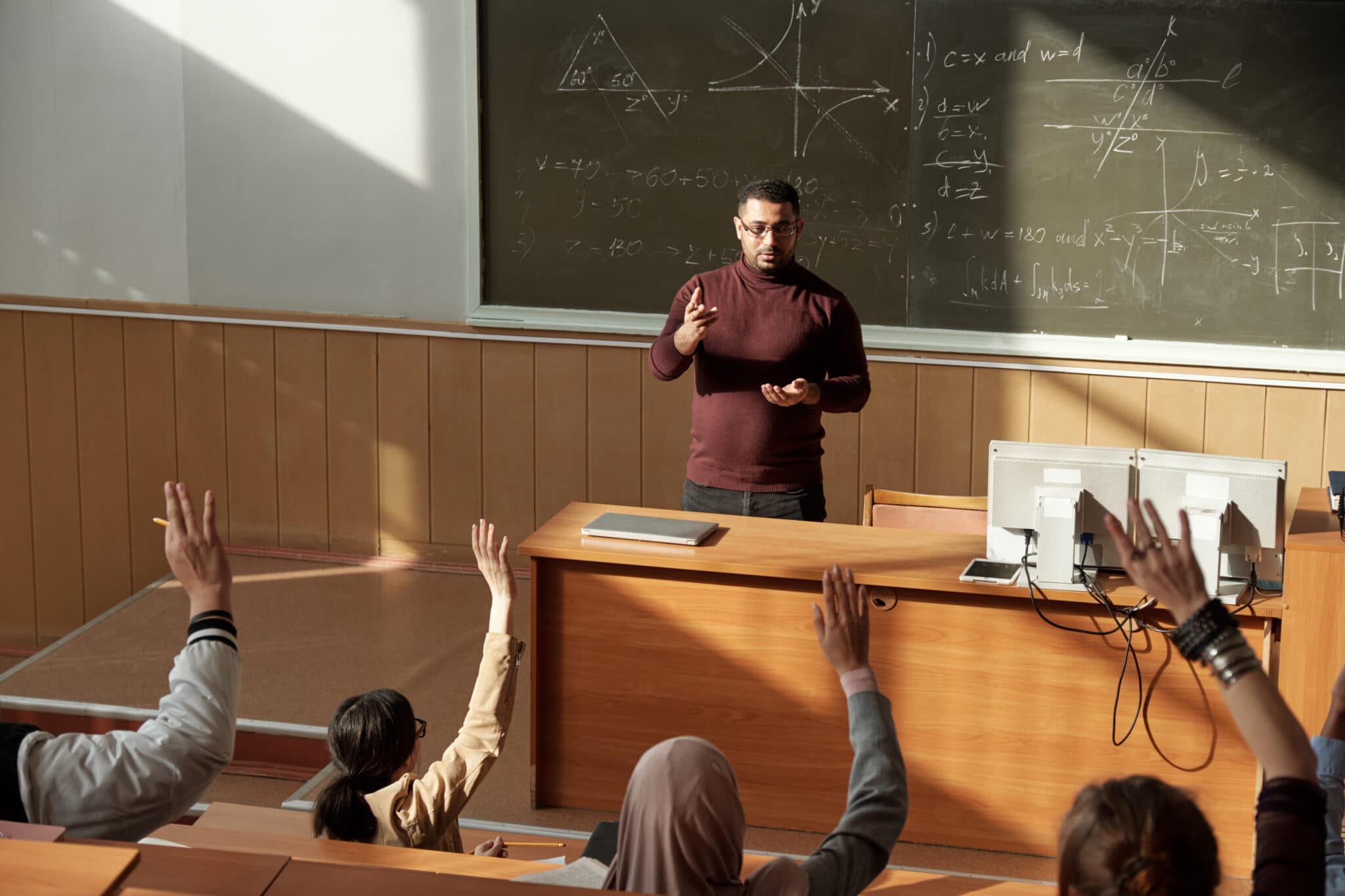Middle aged teacher in casualwear standing by blackboard in lecture hall and lecturing students. Picture embodies a lesson about administrative appointments.