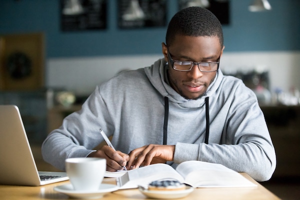 Focused Black student making notes while studying in cafe